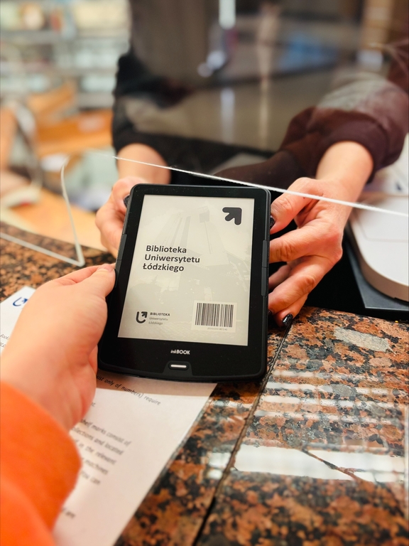 Czytnik e-booków przekazywany czytelniczce przez pracowniczkę wypożyczalni.