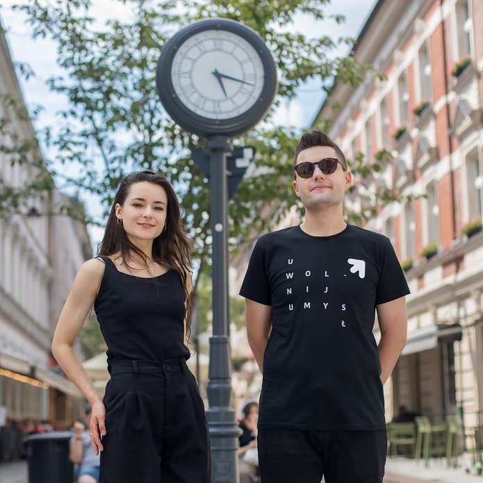 Ciemnowłosa dziewczyna i chłopak w czarnych koszulkach na tle ulicznego zegara