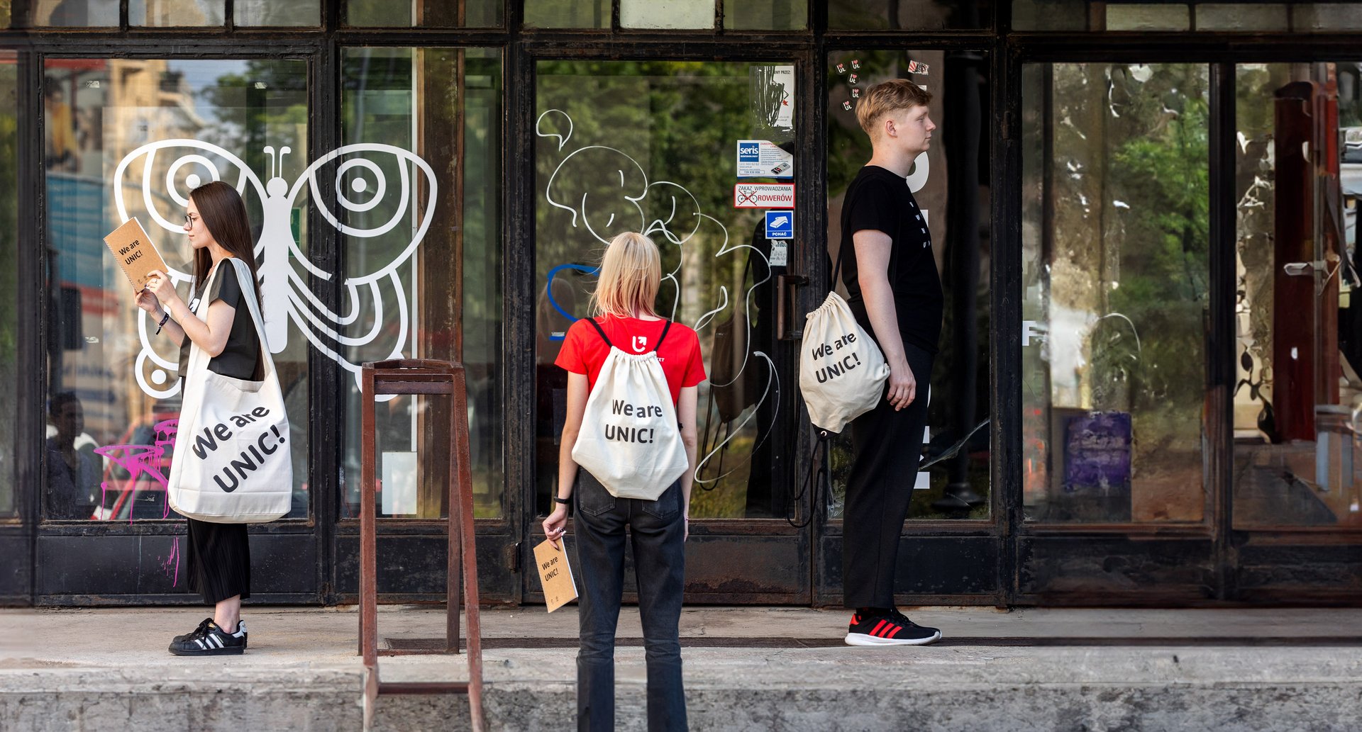 Troje studentów stojących na schodach z torbami i plecakami z projektu UNIC