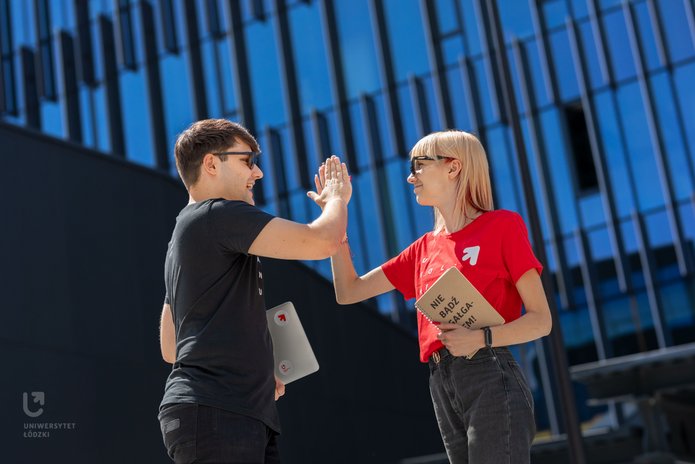 Młoda kobieta  z notesem w dłoni i mężczyzna z komputerem w dłoni przybijają sobie piatkę