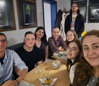 Grupa studentów i studentek lekko uśmiechniętych. Siedzą przy stoliku w restauracji.
