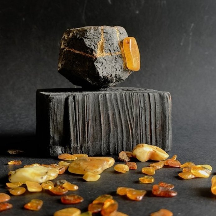 Na zdjęciu widać rozsypane bursztyny oraz kamień lub ceramikę w kształcie sześcianu w kolorze czarnym.
