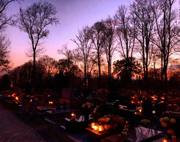 widok cmentarza o zmierzchu, z płonącymi na grobach zniczami