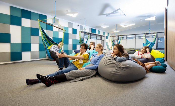 Zdjęcie wnętrza sali relaksu w CWiD UŁ. Na hamakach i pufach siedzą uśmiechnięci młodzi ludzie