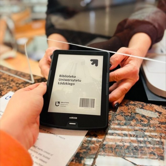 Czytnik e-booków przekazywany czytelniczce przez pracowniczkę wypożyczalni.