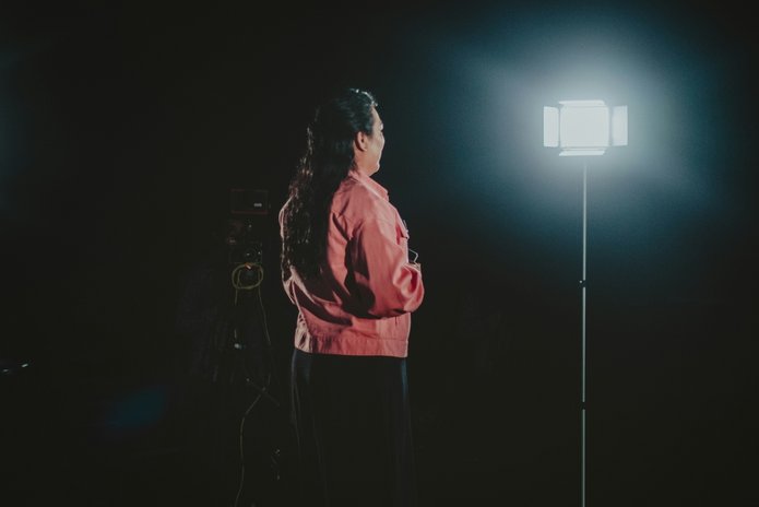 A woman giving a speech in front of a camera and a lamp