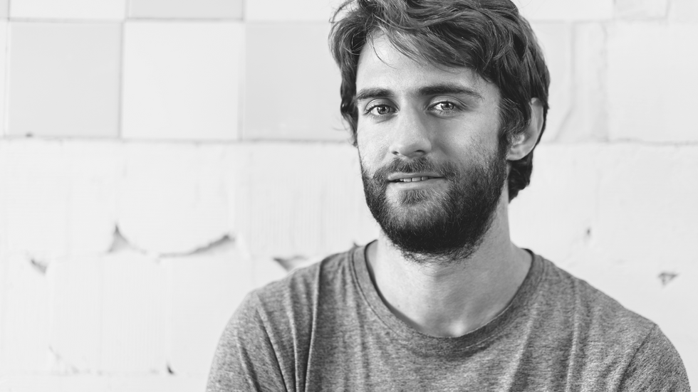 a decorative element: a black and white photo of a smiling young man with a beard looking straight into the camera