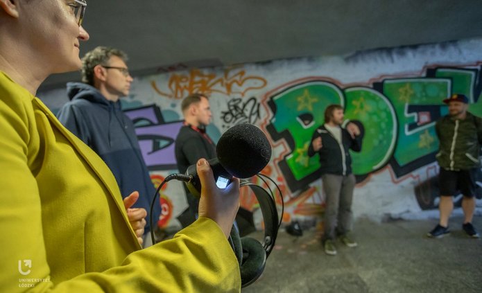 Na zdjęciu widać grupę ludzi. Stoją przejściu podziemnym. Trzymają w rękach urządzenia do nagrywania dźwięków.