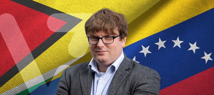 Zdjęcie portretowe dr Mateusza Piątkowskiego na tle flag Wenezueli i Gujany