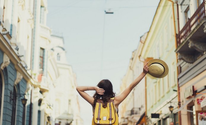 Back view of a young woman traveler with a backpack on her shoul Dziewczyna na wakacjach zwiedza miasto z kapeluszem w ręce