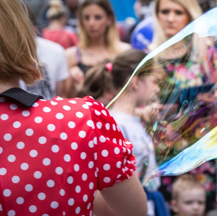 A woman wearing a red dress with white polka dots with soap bubbles, other people visible in the background